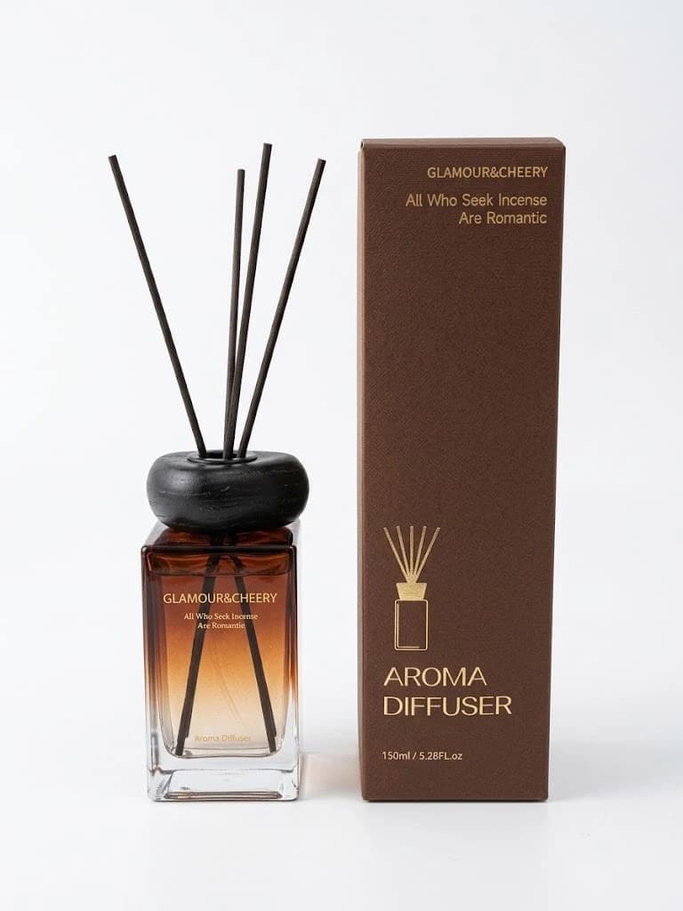 معطر جو زجاج مستطيل بسائل بني وأعواد سوداء بجانب علبة بنية، على خلفية بيضاء.